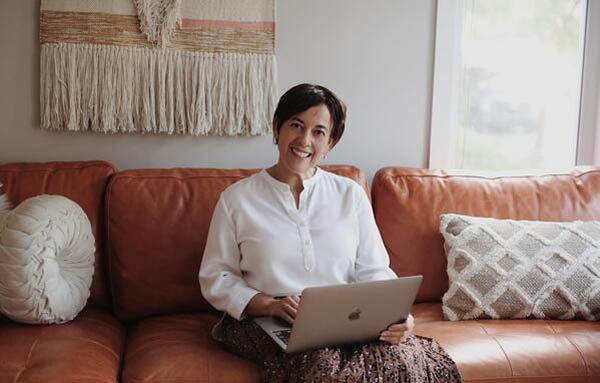 Female business person sitting on couch smiling while looking up from laptop