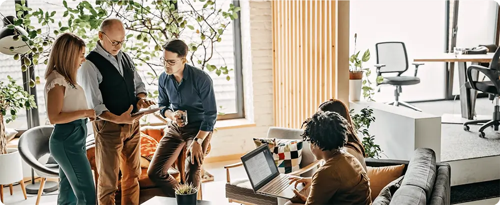 Diverse group of professionals discussing work in a modern office with plants and natural light.