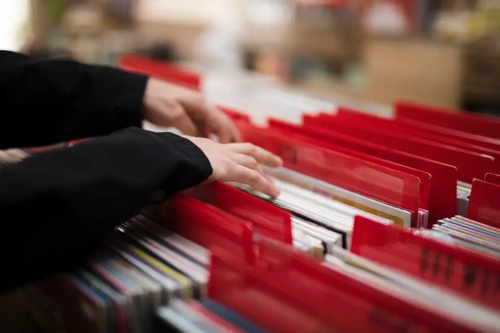 Hands browsing through vinyl records or documents organized in red file dividers at a store or library.