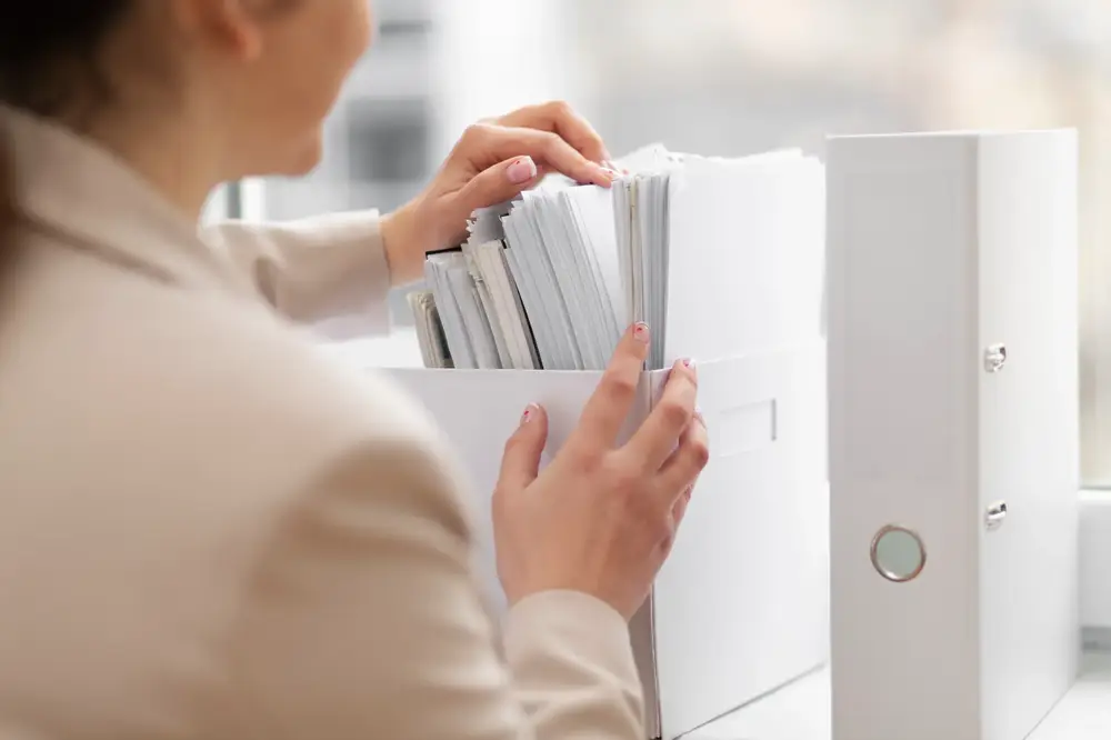 Woman organizing or searching through a white box filled with documents, with a binder beside her.